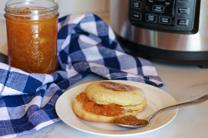 English muffin on white plate with peach jam spread; Crockpot Express in background