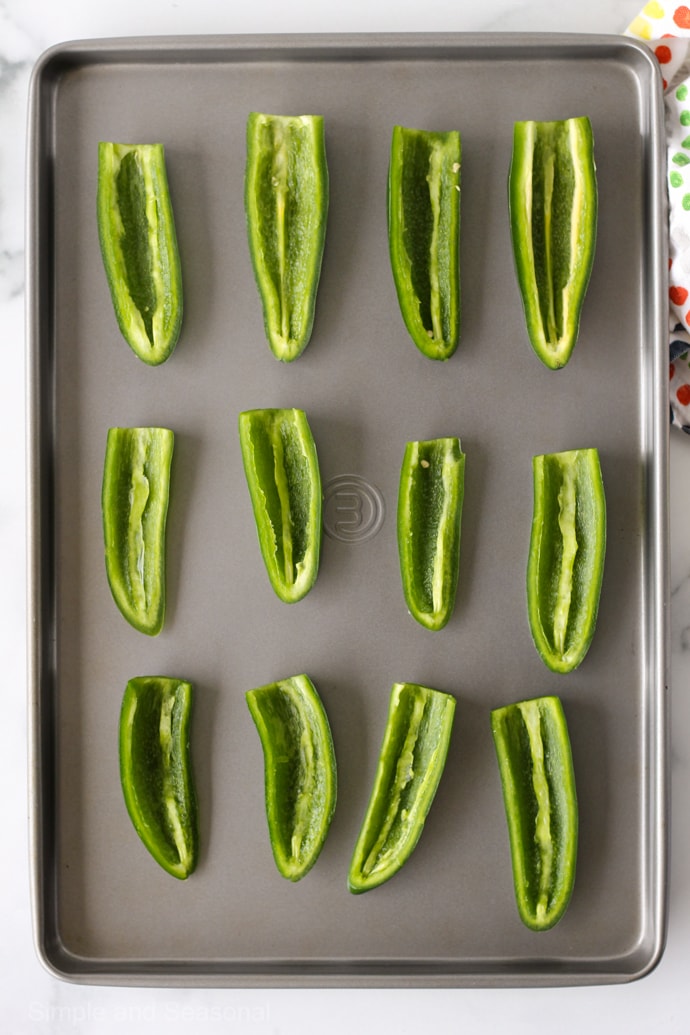 top down view of baking sheet with 12 jalapeno halves, ribs and seeds removed