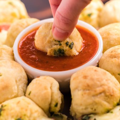 hand dipping pizza monkey bread into dipping sauce