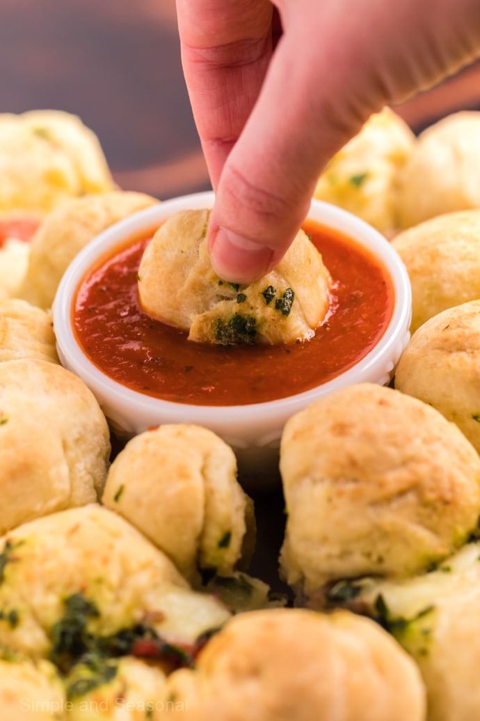 hand dipping pizza monkey bread into dipping sauce