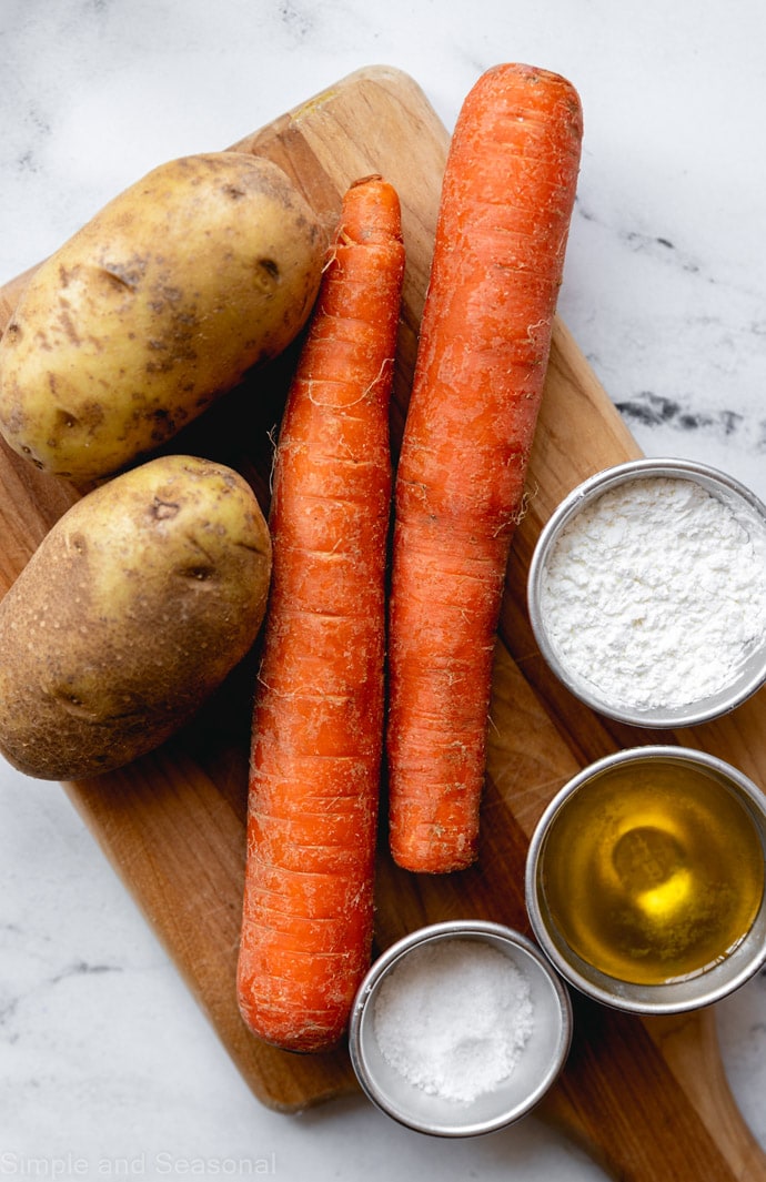 raw carrots, potatoes, oil, salt and cornstarch on a cutting board