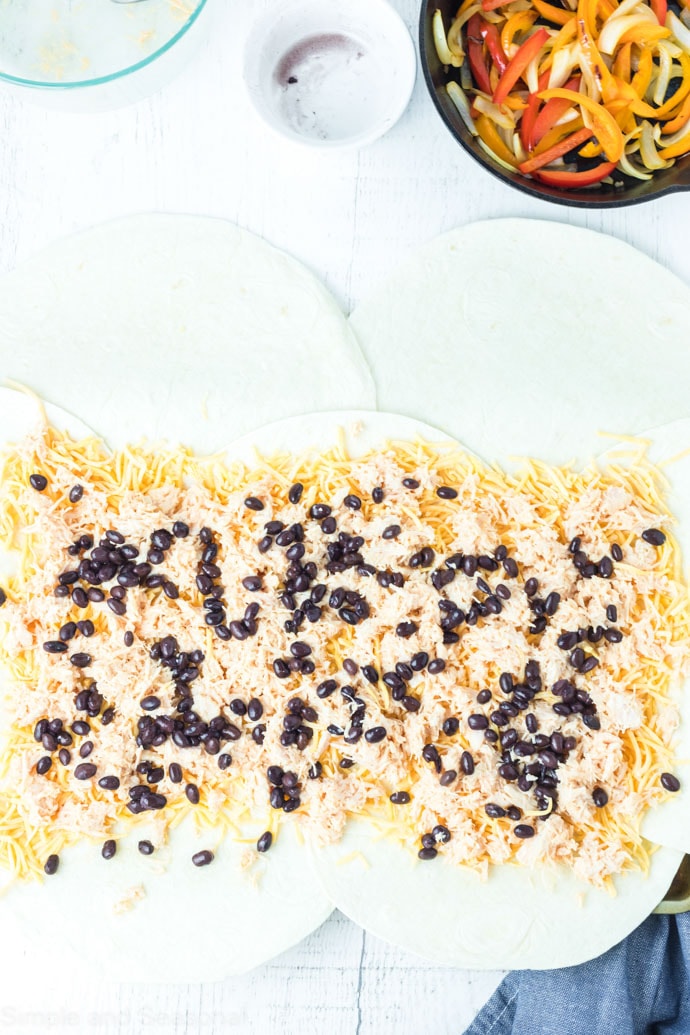 beans, chicken and cheese on open tortillas in a sheet pan