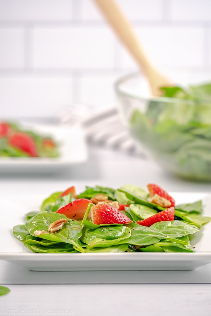 white plate with spinach strawberry salad and salad bowl in background