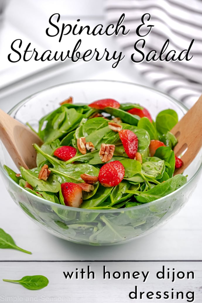 salad in a salad bowl with two wooden tongs; text label reads: Spinach and Strawberry Salad with honey dijon dressing