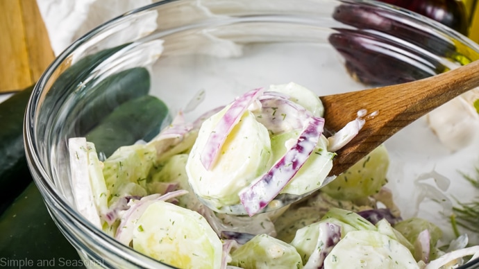 bowl of creamy cucumber salad with wooden spoon