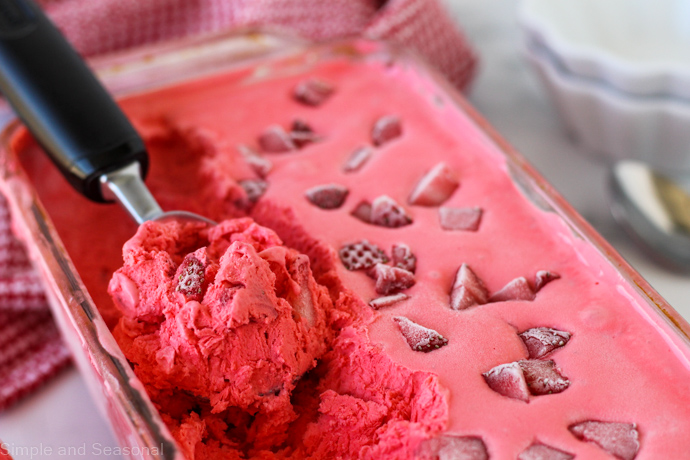 strawberry ice cream in a loaf pan with a scoop rolled up into the spoon
