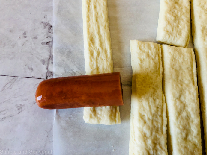 hot dog piece being wrapped up in a strip of dough