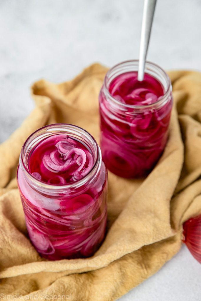 two jars of pickled red onions on a yellow kitchen towel