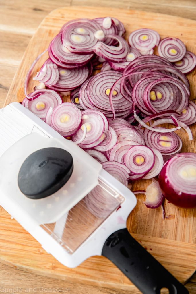 cutting board covered in sliced red onions and mandolin slicer