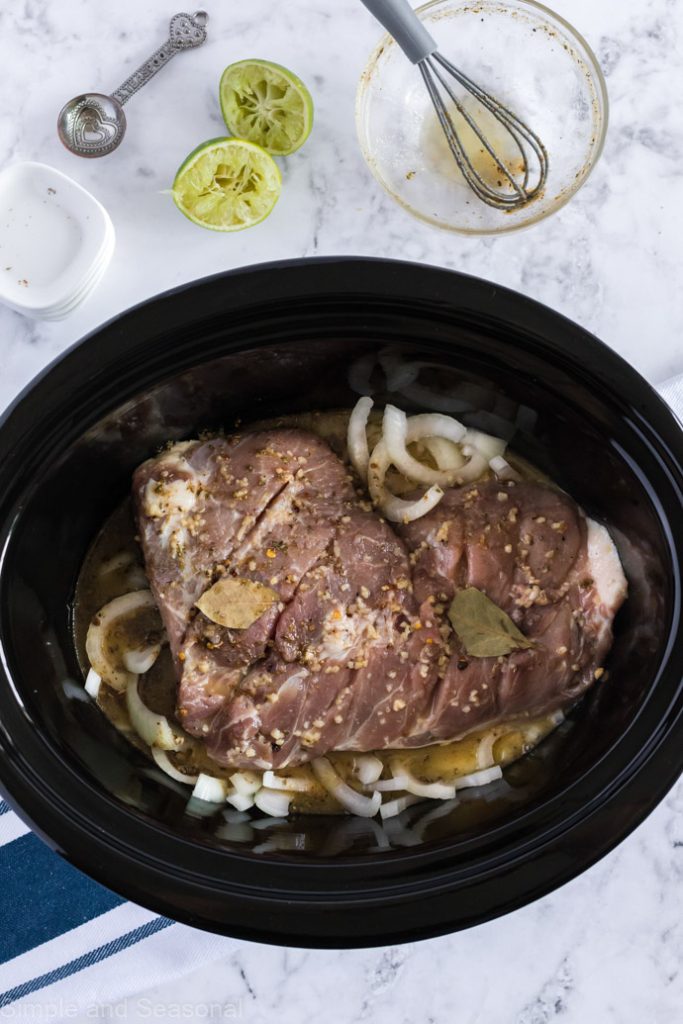 pork roast placed in slow cooker on top of onion slices with seasoning mixture poured over the meat