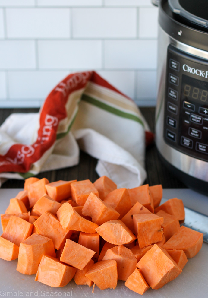 chopped sweet potatoes (garnet yams) on a cutting board with pressure cooker in the background