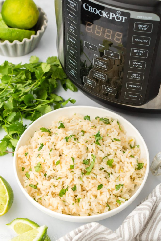 bowl of cilantro lime rice with limes, cilantro and crockpot express on the table
