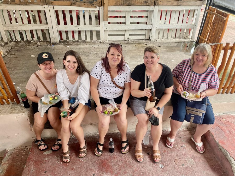 ladies lined up on a wall eating carnitas tacos