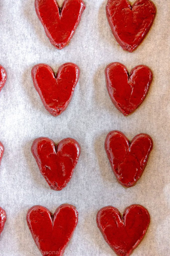 red hearts piped onto a parchment lined baking sheet