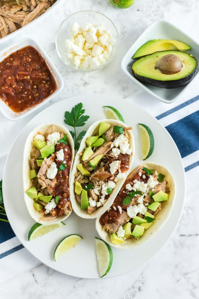 three stuffed taco shells on a white plate with taco toppings around the top