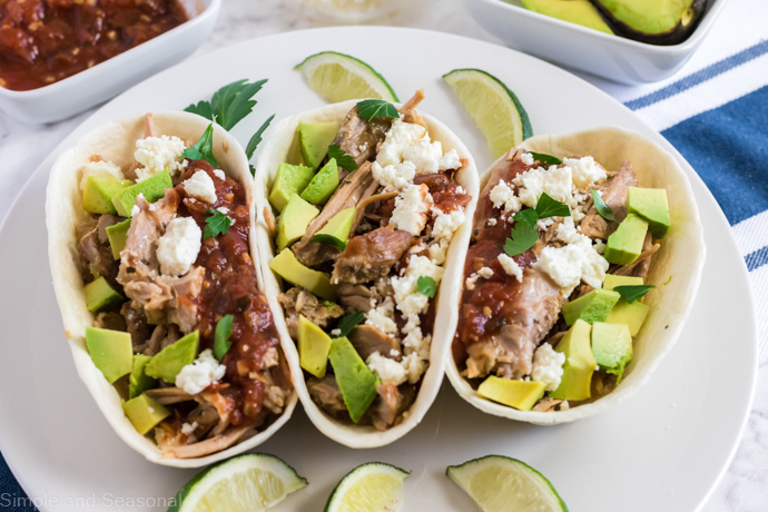 close up shot of taco shells holding pork and other toppings with lime wedges as garnish