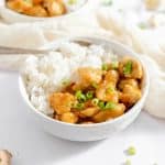 white bowl filled with white rice and sweet and spicy chicken topped with green onionsh