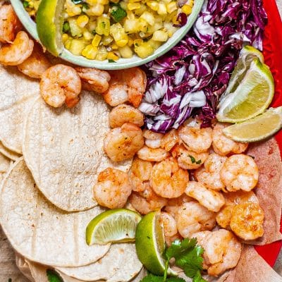 sweet and spicy shrimp with tortillas, cabbage, lime wedges and corn salsa