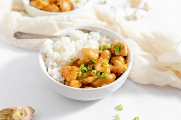 piece of ginger and green onions near bowl of white rice with spicy and sweet chicken