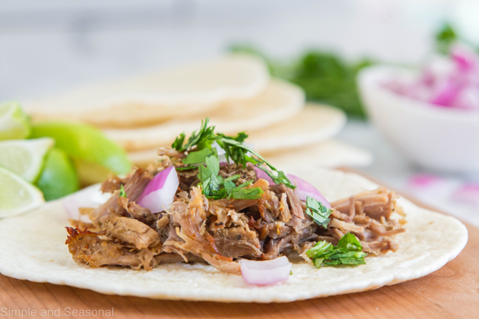close up of carnitas; stack of tortillas in the background