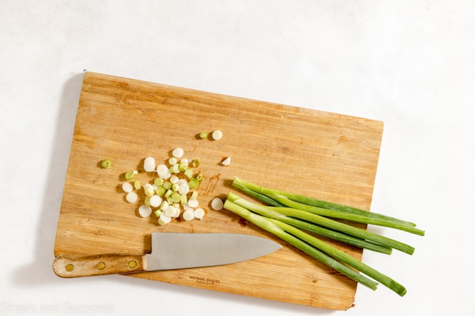 green onions on a chopping board with knife