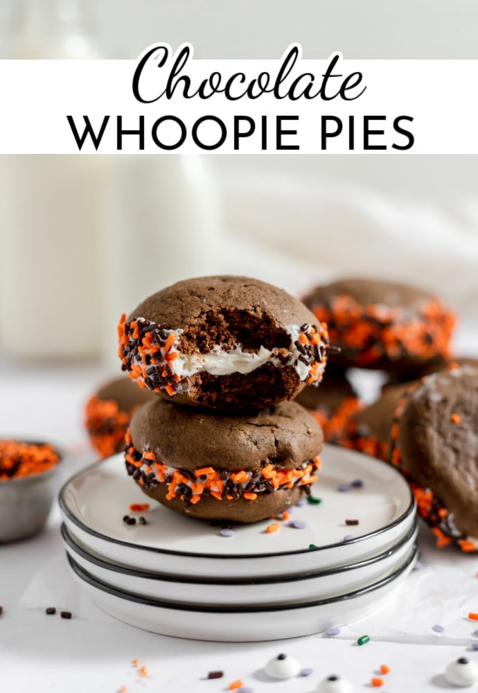 two chocolate whoopie pies on a stack of plates, one with bite taken out and cream filling showing.