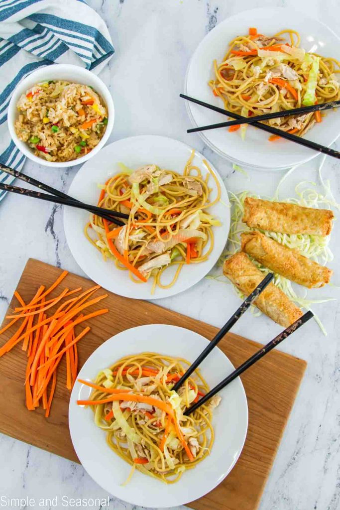 top down view of plates of chicken lo mein, fried rice and egg rolls