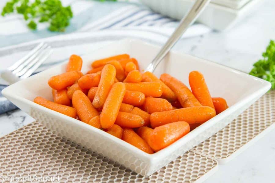 square bowl of carrots with serving spoon and brown placemat
