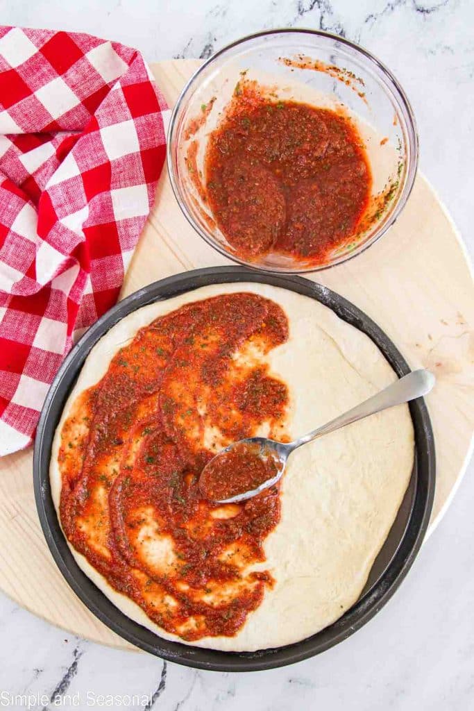 pizza dough being spread with red pizza sauce