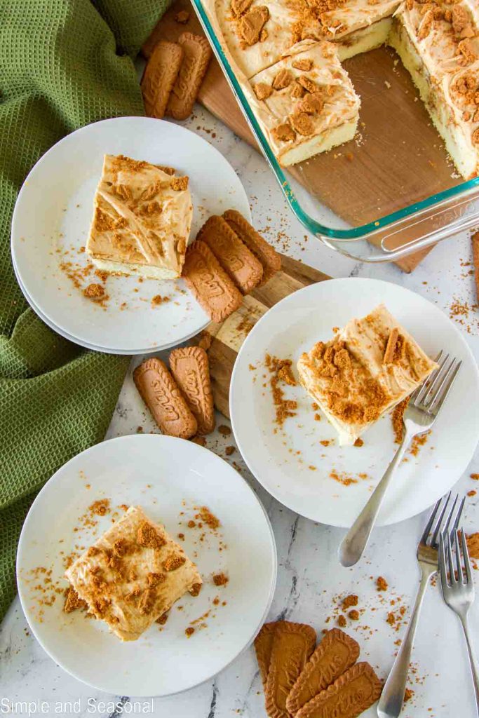 top down view of cake in pan and slices on plates, surrounded by Lotus Biscoff cookies