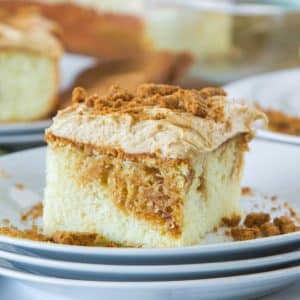 square slice of cake topped with frosting and crumbled cookies on a stack of dessert plates