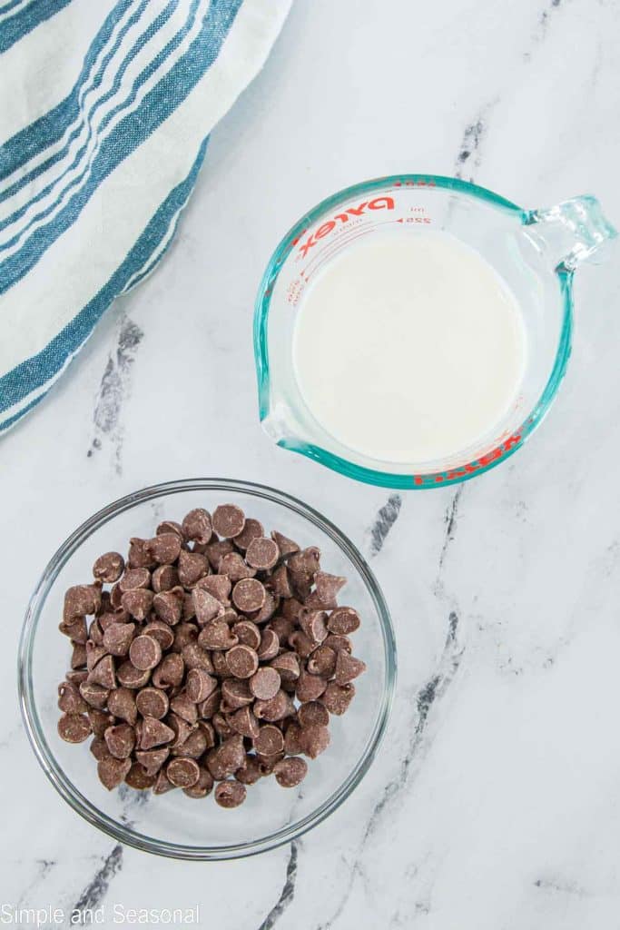 measuring cup with heavy cream and glass bowl with chocolate chips