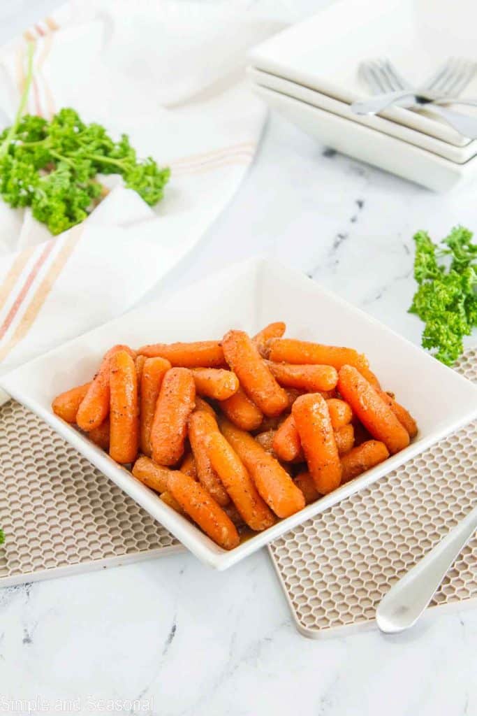 bowl of cooked spicy carrots with extra plates and forks in the background