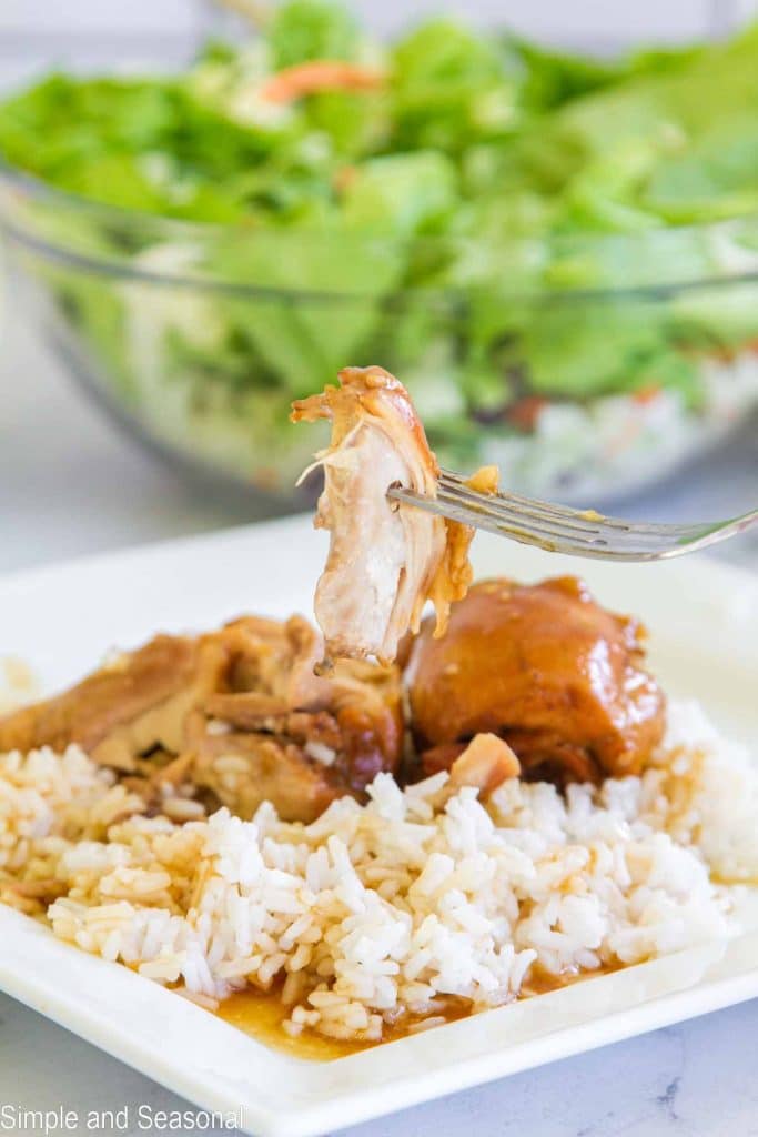 forkful of Crockpot Express Teriyaki Chicken with plate of rice and sauce