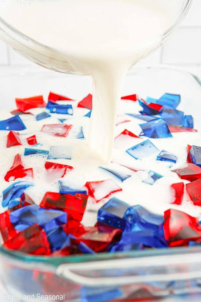 white milk mixture being poured over red and blue gelatin cubes