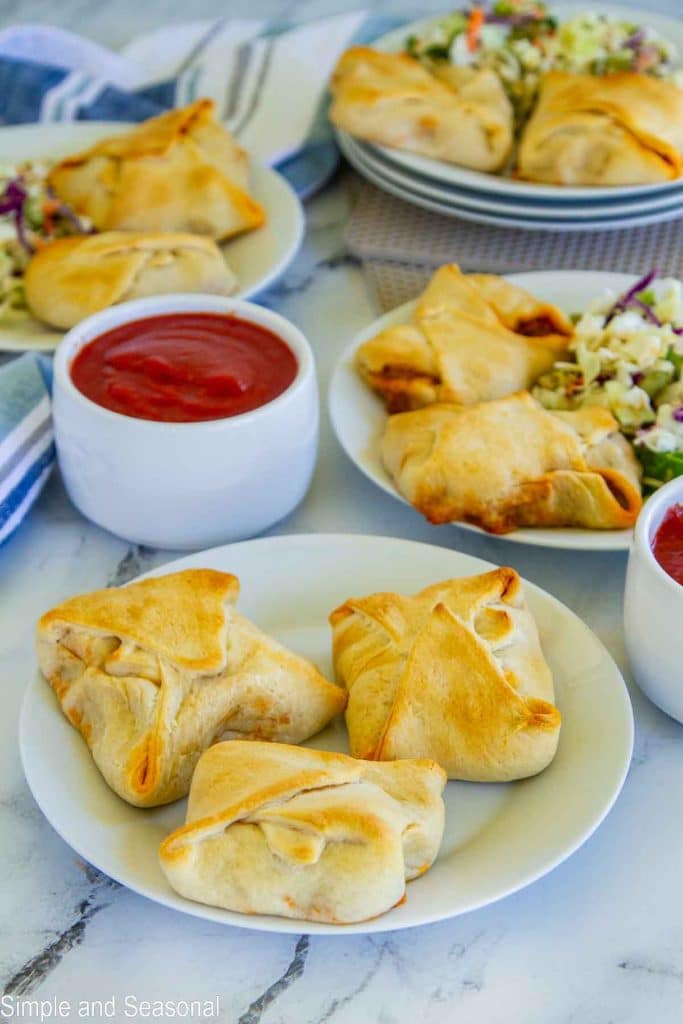 several plates of homemade pizza pockets and salad with extra dipping sauce on a table