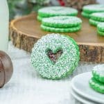 close up of green cookie with heart cut out and raspberry jam leaning against a wooden platter