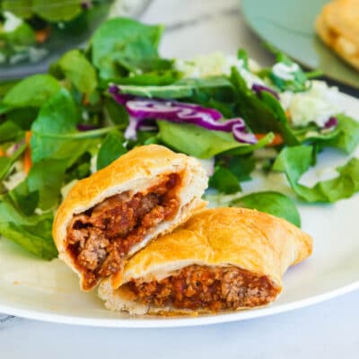 cut open biscuit "pocket" stuffed with sloppy joe filling and cheese on a white plate with salad in the background