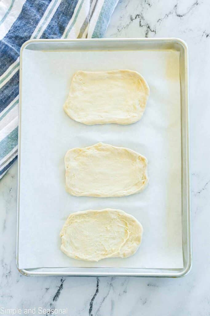 biscuit dough stretched out on a parchment lined cooking sheet.