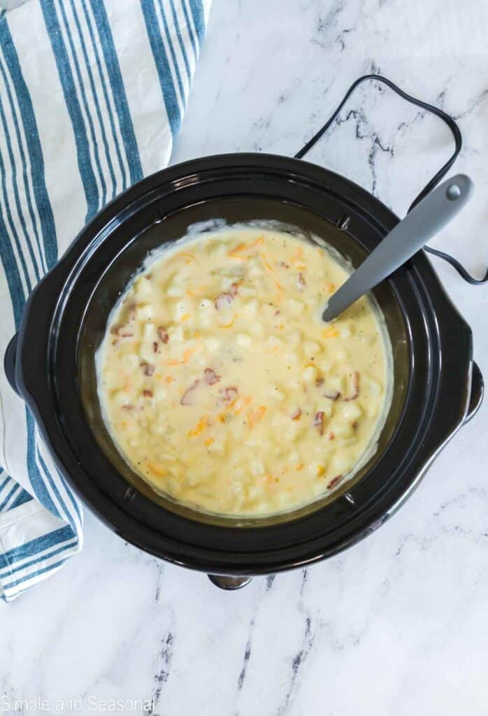 Cooked potato soup with cheese and bacon stirred into the slow cooker.