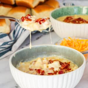 shows spoonful of potato soup over bowl of soup topped with cheese and bacon.