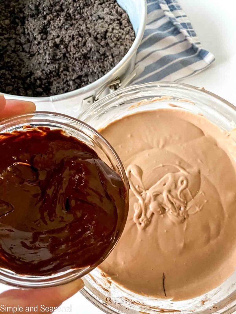 shows small bowl of melted chocolate being added to cream cheese mixture in bowl