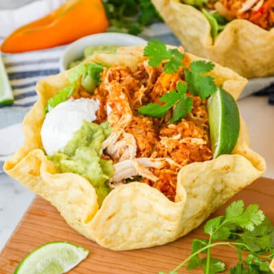 crunchy taco bowl filled with shredded chicken, rice and topped with sour cream and guacamole