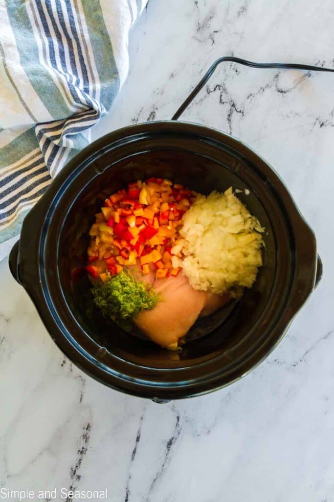bowl of slow cooker filled with chicken breast and peppers and onions