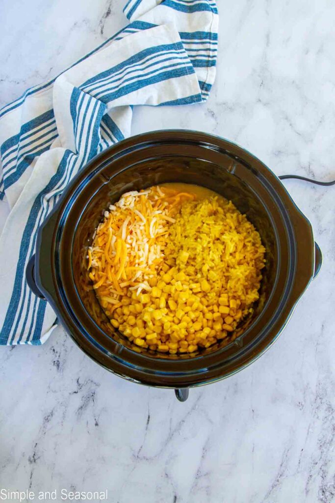 rice, corn and cheese added to the cooked chicken in the crockpot