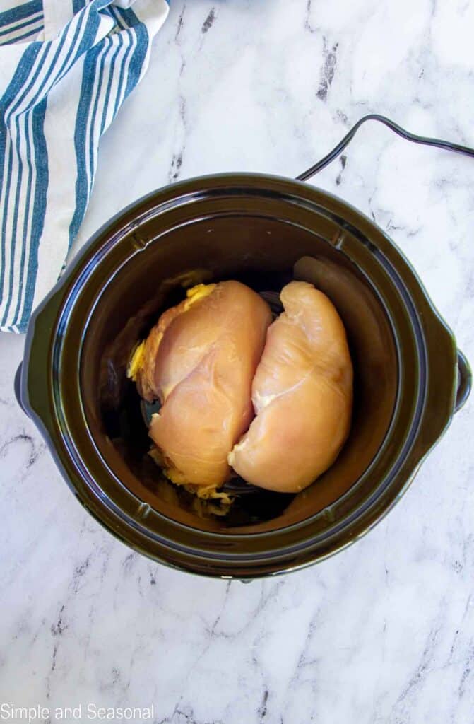 raw chicken breasts in the bottom of a slow cooker