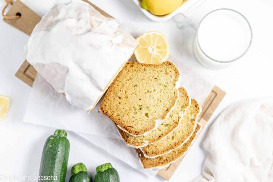 loaf of baked and glazed lemon zucchini bread on cutting board with slices cut