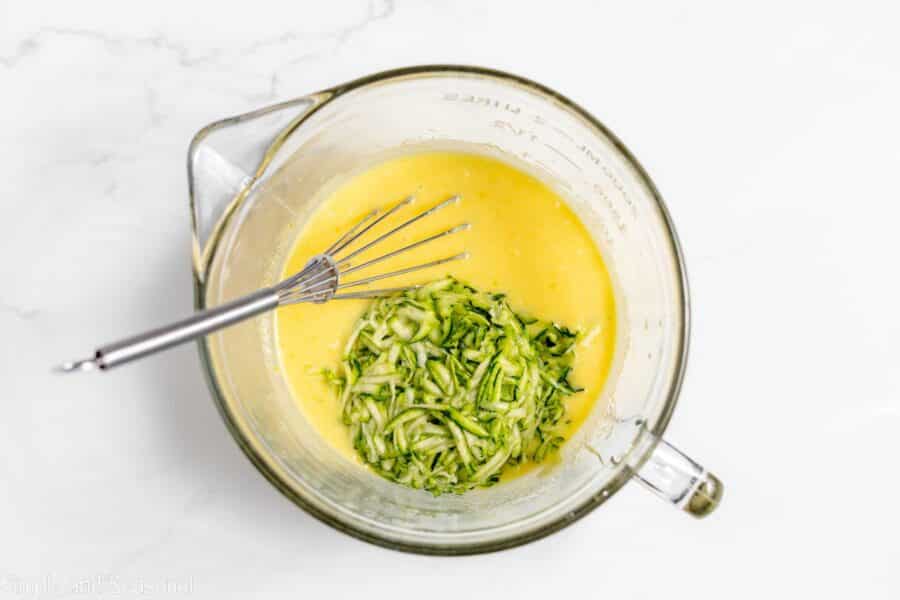 grated zucchini added to mixing bowl with whisked sugar and egg mixture