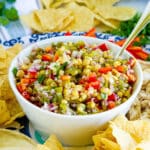 close up on white bowl of roasted corn salsa with chips for dipping