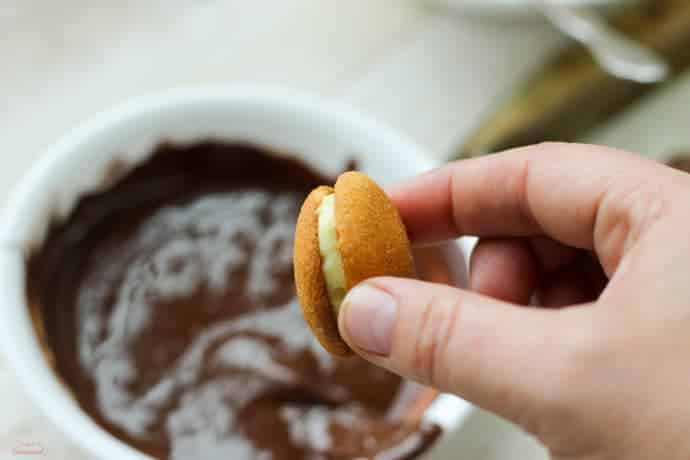 hand holding cookie "sandwich" getting ready to dip in melted chocolate